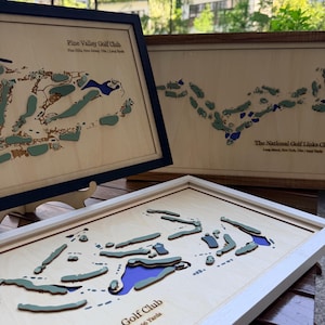 Puede incluir: Tres mapas de madera en 3D enmarcados de campos de golf. El mapa superior izquierdo es Pine Valley Golf Club, el superior derecho es The National Golf Links Club y el inferior muestra un diseño de campo de golf con agua azul y calles verdes.