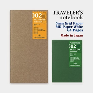 Puede incluir: Dos cuadernos Traveler's, uno marrón y otro verde. El cuaderno marrón tiene una etiqueta que dice "002 Traveler's notebook" con "5x5 mm Grid" y "64 páginas". El cuaderno verde es de tamaño pasaporte. El texto "Made in Japan" es visible.