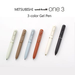 May include: A collection of six uni-ball One 3-color gel pens in various colors, including off-white, brown, light blue, rust, cream, and black. The pens are arranged on a white surface, with the product name and description visible.