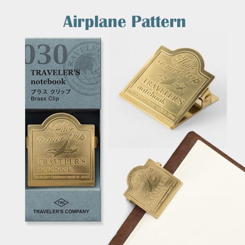 May include: Brass clip for a Traveler's notebook with an airplane design. The clip is gold-colored and features the text "Have a nice trip" and "Traveler's notebook". The product is packaged in a blue box with the text "Airplane Pattern".
