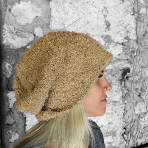 May include: A fluffy, beige knit beanie hat with a slouchy fit. The hat is made of a soft, textured yarn and has a simple, classic design.