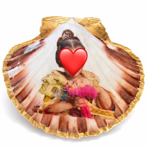 Può includere: Una conchiglia di capasanta con il bordo dipinto in oro che presenta un'immagine stampata di una persona in abito formale che tiene un bouquet rosa, con un'emoji di cuore rosso che copre il viso, centrata all'interno della conchiglia naturale.