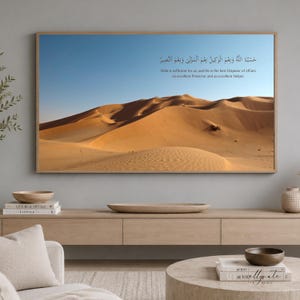 Könnte beinhalten: Ein rechteckiger Wandkunstdruck, der eine weite Wüstenlandschaft mit goldenen Sanddünen unter einem klaren blauen Himmel zeigt. Das Bild enthält arabische Kalligrafie und den englischen Text: Allah is sufficient for us, and He is the best Disposer of affairs.