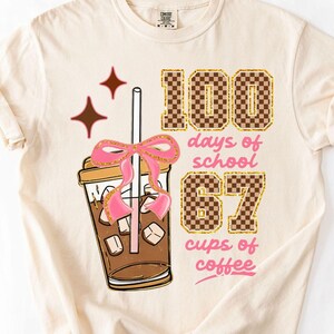 May include: Cream-colored t-shirt featuring a graphic of an iced coffee with a pink bow and the text "100 days of school 67 cups of coffee." The numbers and text are in a checkered pattern.