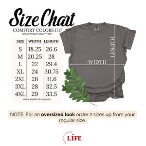 Op de afbeelding: Een maattabel voor Comfort Colors 1717 heavyweight volwassen T-shirts. De tabel toont afmetingen in inches voor maten S tot 4XL. De afbeelding bevat ook een grijs T-shirt en een opmerking over het bestellen.