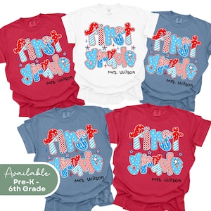 May include: Four different color t-shirts with the text "First Grade" in red, white, and blue with stars. The text is in a playful font and the shirts are available in red, white, blue, and heather blue.