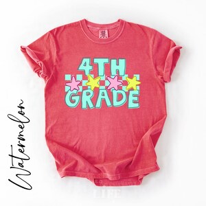 May include: A red t-shirt with the words "4th Grade" in turquoise and white, with pink and yellow stars. The word "Watermelon" is written in cursive on the left side of the shirt.