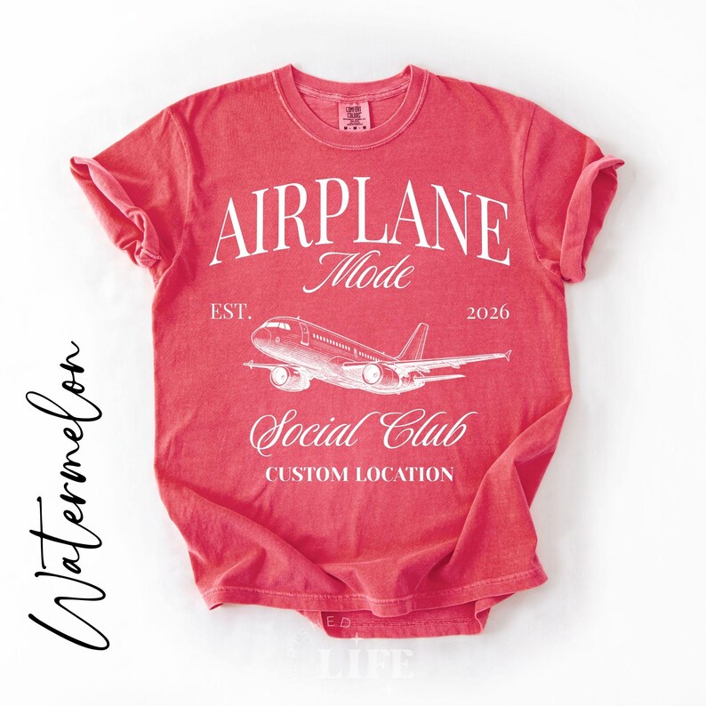 Puede incluir: Una camiseta roja con las palabras "AIRPLANE Mode" en blanco y un gr&aacute;fico de avi&oacute;n. Debajo del gr&aacute;fico, se lee "Social Club" y "Custom Location". La camiseta tambi&eacute;n tiene el texto "EST. 2026". La palabra "Watermelon" est&aacute; escrita al lado.