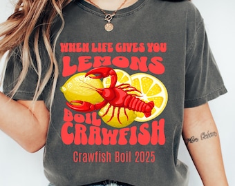 May include: A gray t-shirt with the text "When life gives you lemons, boil crawfish" in red and yellow. The shirt also has a red crawfish illustration and the text "Crawfish Boil 2025" in red.