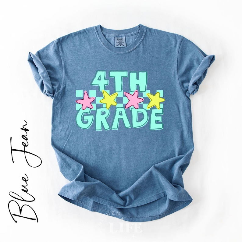 May include: Blue jean t-shirt with the words "4TH GRADE" in a turquoise font with pink and yellow stars. The shirt is a light blue color and has rolled-up sleeves.