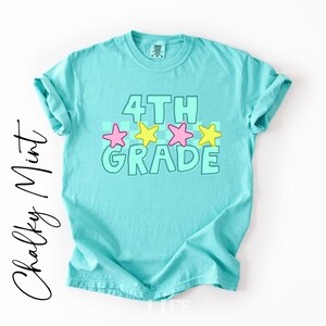 May include: A turquoise t-shirt with rolled-up sleeves. The front features the words "4TH GRADE" in a light green outline, with pink and yellow stars. The words "Chalky Mint" are written in a cursive font on the left side.