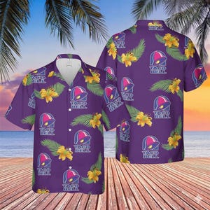 May include: Purple button-down shirt featuring a repeating pattern of the Taco Bell logo, yellow flowers, and green leaves. The shirt has short sleeves and a white collar. The background shows a beach scene with palm trees.