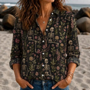 May include: A long-sleeved button-down shirt in a dark charcoal color featuring a repeating pattern of white human skeletons interspersed with various pink, yellow, and green botanical floral elements and green foliage throughout the fabric.