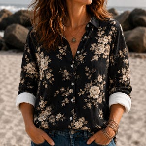 May include: A long-sleeved button-down shirt in black featuring a beige floral pattern. The shirt has a classic collar, white buttons down the front, and cuffs that are rolled up to reveal a solid white interior lining, paired with blue denim jeans.