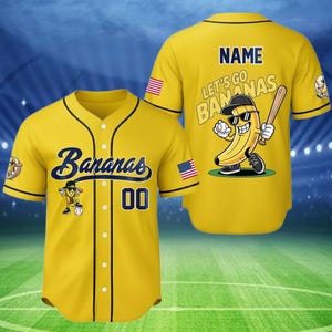 Puede incluir: Camiseta de b&eacute;isbol amarilla con ribete negro. La parte delantera muestra la palabra "Bananas" en escritura azul marino. La camiseta tiene un personaje de pl&aacute;tano de dibujos animados y el n&uacute;mero "00". La parte trasera tiene el texto "Let's Go Bananas" y un personaje de pl&aacute;tano con un bate de b&eacute;isbol.