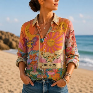 May include: A long-sleeve button-down shirt featuring a vibrant, multi-colored print of celestial motifs, including a large tarot card design labeled THE SUN, a crescent moon, and various floral patterns in shades of orange, pink, yellow, and purple.