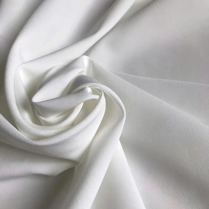 May include: A solid white fabric with a smooth, matte texture, displayed in a series of soft, flowing folds and drapes that create deep shadows and highlights across the surface, emphasizing the clean, uniform color and consistent material weave.