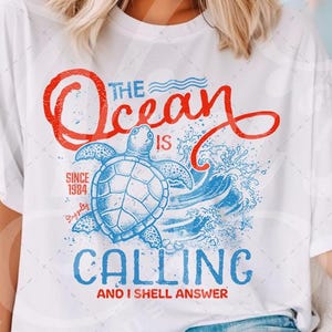 Puede incluir: Camiseta blanca con un gráfico azul y rojo de una tortuga marina y olas. El texto "The Ocean is Calling and I Shall Answer" está impreso en la camiseta.