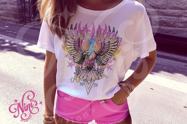 May include: White t-shirt with a graphic of an eagle with the text "Free Bird" and "America 1972" printed on it. The eagle is surrounded by flames and stars.