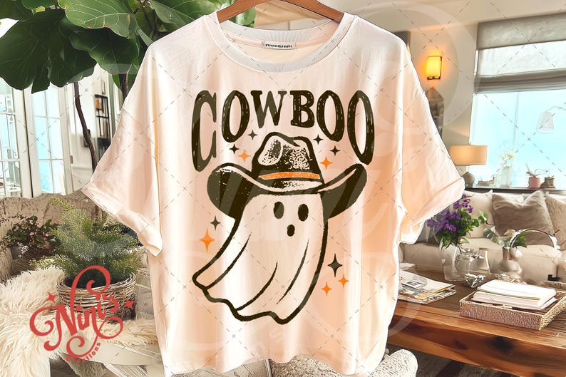 Puede incluir: Camiseta color crema con un dise&ntilde;o de un fantasma con sombrero de vaquero. La palabra "COWBOO" est&aacute; impresa encima del fantasma en una fuente desgastada. Estrellas y detalles en naranja rodean al fantasma y el texto.