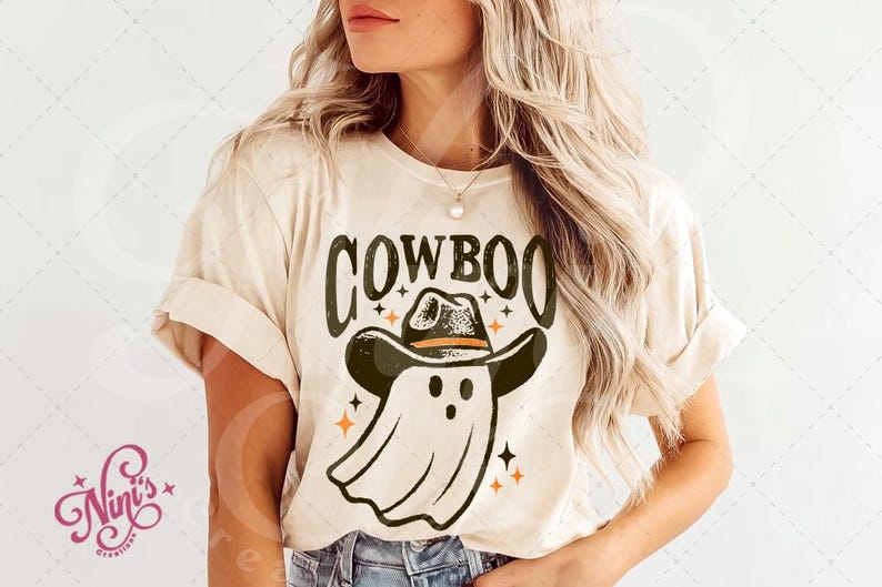 Puede incluir: Camiseta beige con la palabra "COWBOO" en letras verde oscuro. El dise&ntilde;o presenta un fantasma con sombrero de vaquero y estrellas naranjas. Una camiseta gr&aacute;fica con tem&aacute;tica de Halloween.