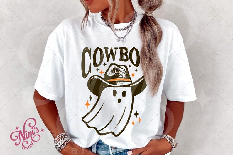 Puede incluir: Camiseta blanca con un gr&aacute;fico que presenta la palabra "COWBO" sobre un fantasma con sombrero de vaquero. El dise&ntilde;o incluye estrellas naranjas. La camiseta es de estilo casual y unisex.