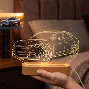 May include: A glowing LED car night light. The car design is etched into a clear acrylic panel, illuminated by a warm light from a wooden base. The car is a modern SUV style. A small photo of the car is in the background.
