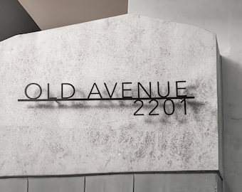 May include: Black metal sign displaying the words "OLD AVENUE" above the number "2201". The sign is mounted on a textured, light gray surface. The background features neutral tones of gray and beige.