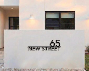 May include: A black metal house number sign mounted on a white wall. The sign features the number 65 positioned above a horizontal line, with the text NEW STREET centered below the line in a clean, sans-serif font, creating a modern appearance.