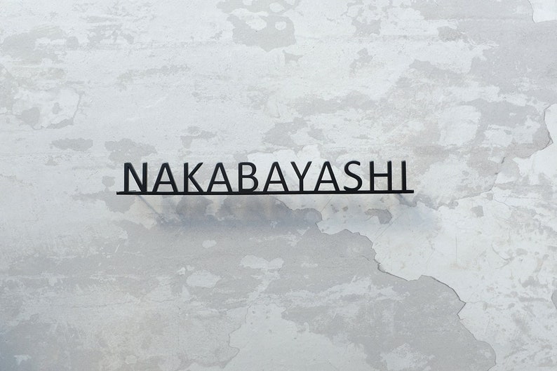 May include: A black metal sign with the text "NAKABAYASHI" on a white textured wall.
