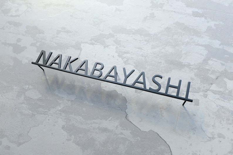 May include: Black metal sign with the name "NAKABAYASHI" in raised letters.