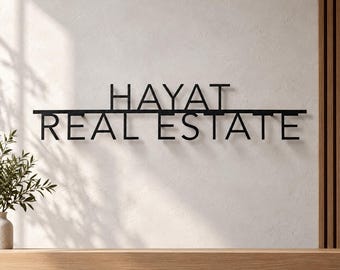 May include: A black metal wall sign featuring the text HAYAT REAL ESTATE in a clean, sans-serif font. The word HAYAT is positioned above the word REAL ESTATE, with a horizontal line separating the two lines of text.
