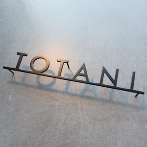Puede incluir: Un letrero de metal negro con la palabra "TOTANI" escrita en may&uacute;sculas.