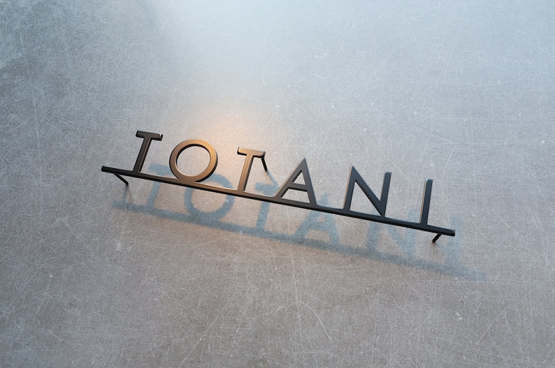 Puede incluir: Un letrero de metal negro con la palabra "TOTANI" escrita en may&uacute;sculas.