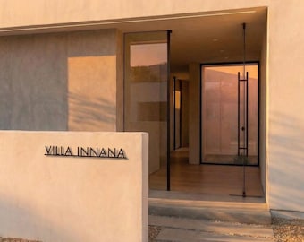 May include: Exterior view of a modern building with large glass doors and windows. The text "VILLA INNANA" is displayed on a white wall. The building has a neutral color palette with warm lighting, creating a welcoming atmosphere.