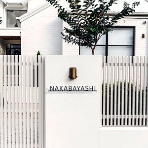 May include: A white picket fence with a gate and a white brick wall with a brass light fixture and a black sign that reads "NAKABAYASHI".