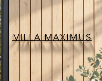 May include: A black metal sign featuring the text VILLA MAXIMUS in a clean, sans-serif font. The letters are connected by a thin horizontal line running along the bottom, creating a unified piece of wall-mounted signage for exterior display.