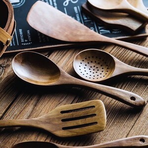 May include: A selection of wooden kitchen utensils, such as spoons, spatulas, and slotted spoons. The light brown wooden tools are displayed on a wooden surface. The image highlights the natural grain and texture of the wood.