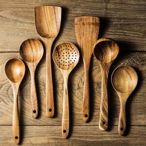 May include: A selection of wooden kitchen utensils, including spoons, spatulas, and a slotted spoon, displayed on a wooden surface. The utensils are crafted from light brown wood, showcasing natural grain patterns. Each has a rounded handle with a hole. The arrangement suggests a culinary theme.
