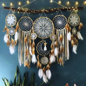 Op de afbeelding: Een handgemaakte wanddecoratie met meerdere dromenvangers. De dromenvangers zijn voorzien van ingewikkelde webontwerpen, versierd met veren, kralen en linten in neutrale tinten. Een maan- en sterontwerp is ook inbegrepen, alles opgehangen aan een tak.