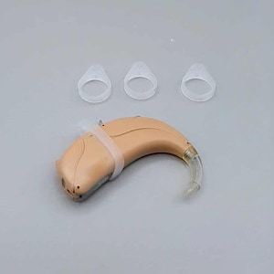 Puede incluir: Un audífono beige detrás de la oreja con un tubo transparente y tres pequeños tapones para los oídos de silicona transparentes.