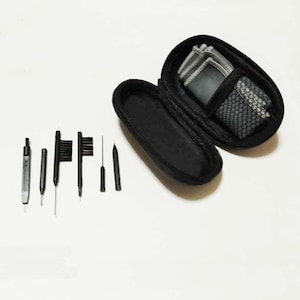 May include: A black carrying case with a zipped opening, containing a set of cleaning tools for spectacles. The tools include a small brush, a metal scraper, and several pointed tools.