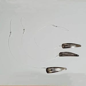 May include: Three hair extension clips featuring a dark brown and black tortoiseshell pattern. Each metal snap clip is attached to a thin, transparent nylon fishing line, with a small loop at the end of each line for secure attachment to hair.