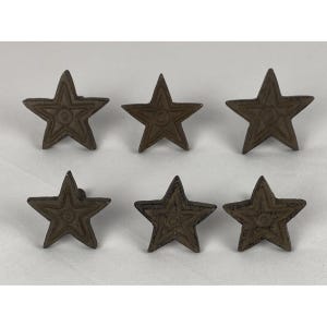 May include: A set of six dark brown, star-shaped metal knobs arranged in two rows of three. Each knob features a raised, five-pointed star design with a circular center detail and textured, weathered surfaces, designed for cabinet or drawer hardware.