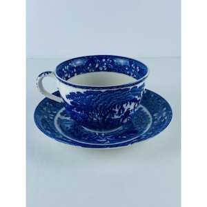 May include: Blue and white porcelain teacup and saucer set. The cup and saucer feature a detailed landscape design with trees and figures. The rim of the cup is decorated with a floral pattern. The set is made of porcelain.