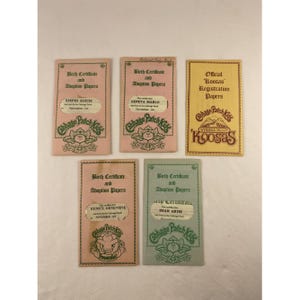 May include: Five vintage Cabbage Patch Kids birth certificates and adoption papers. The certificates are pink, yellow, and blue with the Cabbage Patch Kids logo and names like Stephie Alecia and Geneva Marlo.
