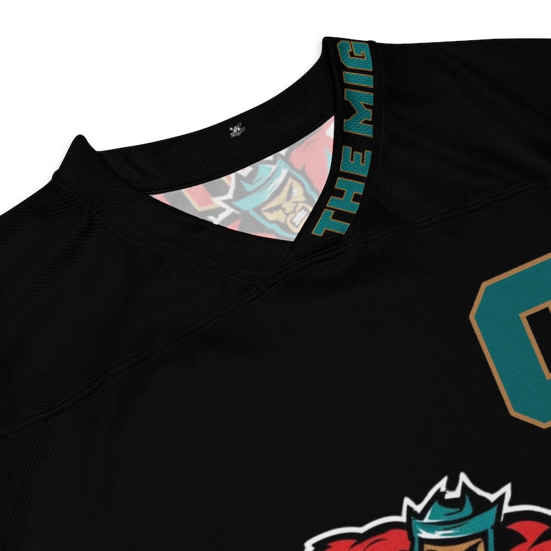 May include: Black jersey with a teal and gold design. The text "THE MIGHT" is on the collar. The jersey has a teal number "0" on the front.