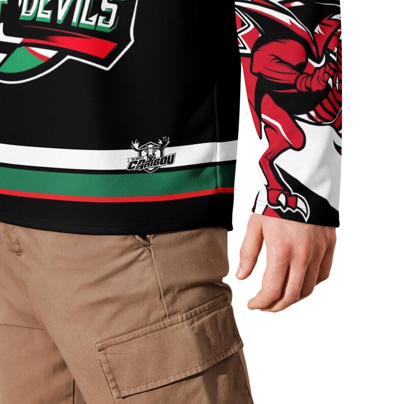 May include: Black hockey jersey with green and red stripes, a red dragon graphic on the sleeve, and the text "The Caribou" on the front.