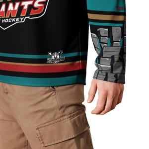 May include: A black hockey jersey with teal, red, and gold stripes. The jersey has the words "Caribou Giants" and "Hockey" on the front. The sleeve has a graphic of a rocky mountain scene.