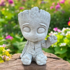 May include: A gray concrete figurine of a character from the movie Guardians of the Galaxy, Groot, standing on a wooden stump. The figurine is in a garden setting with flowers in the background.